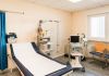 Behandlungsraum einer Arztpraxis mit Untersuchungsliege, Ultraschallgerät, Belastungs-EKG und einem Defibrillator (AED) an der Wand.